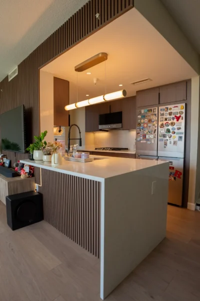 Modern kitchen with waterfall island, wood slat paneling, and stainless steel refrigerator with magnets