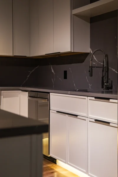 Close-up of modern kitchen sink area with white cabinets and dark marble backsplash