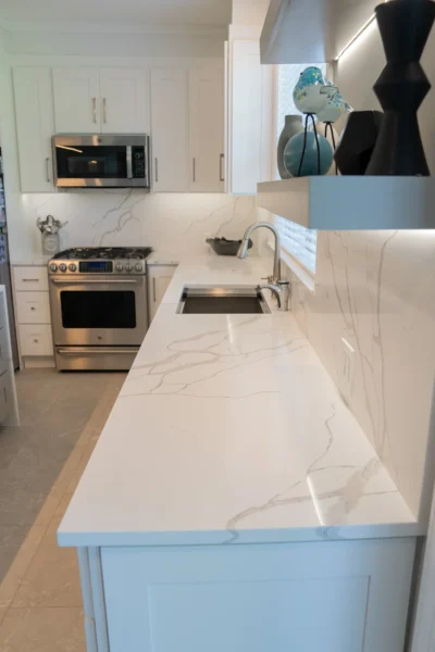 Bright white kitchen with marble countertops, stainless steel appliances, and open shelf decor