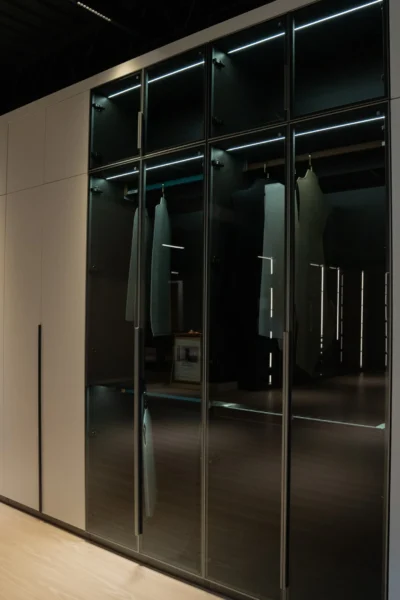 Modern custom closet with glass doors, hanging racks, and ambient lighting