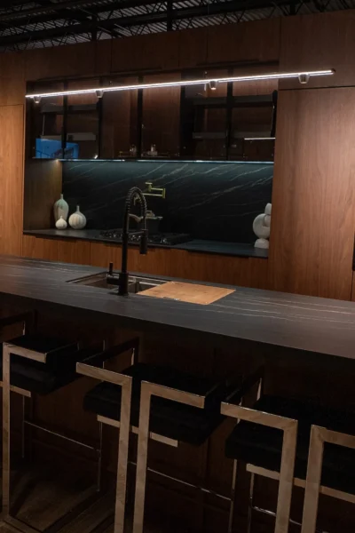Dark luxury kitchen with black stone island, wood cabinetry, and modern bar stools