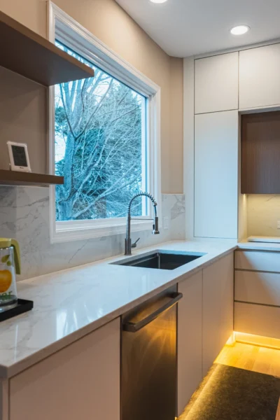Modern kitchen with white cabinets, marble countertops, and window above sink